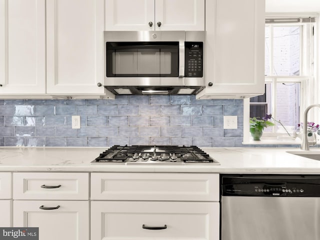 kitchen with tasteful backsplash, a sink, light stone counters, white cabinets, and stainless steel appliances
