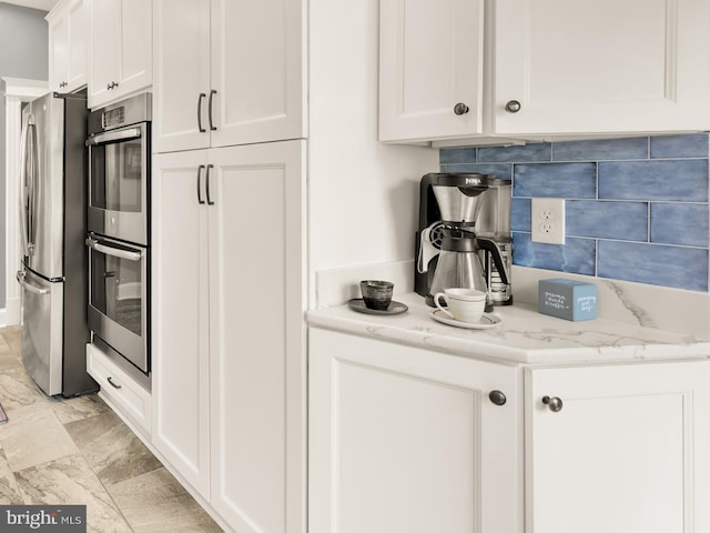 kitchen featuring white cabinetry, light stone countertops, appliances with stainless steel finishes, and decorative backsplash