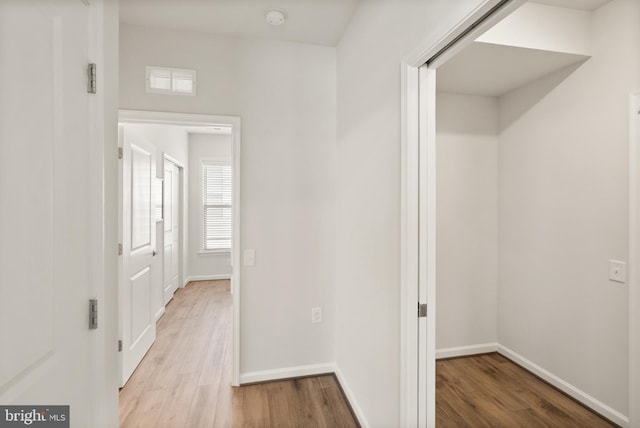 hallway with baseboards, a wealth of natural light, and light wood-style floors