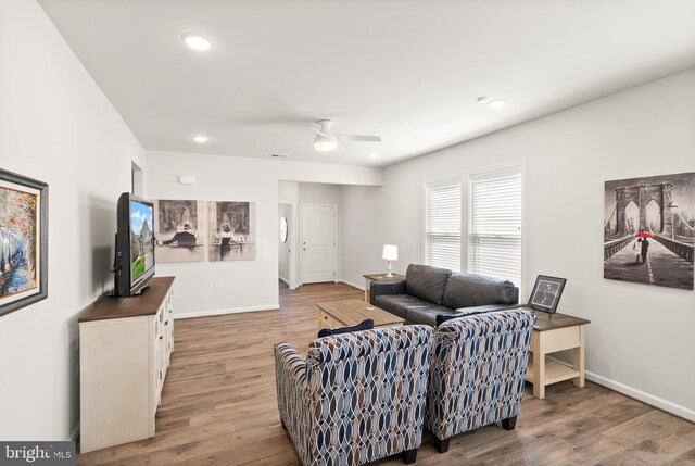 living room featuring baseboards, light wood-style flooring, and ceiling fan