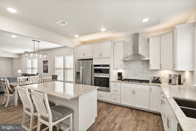 kitchen featuring wall chimney range hood, a kitchen bar, white cabinetry, backsplash, and stainless steel appliances