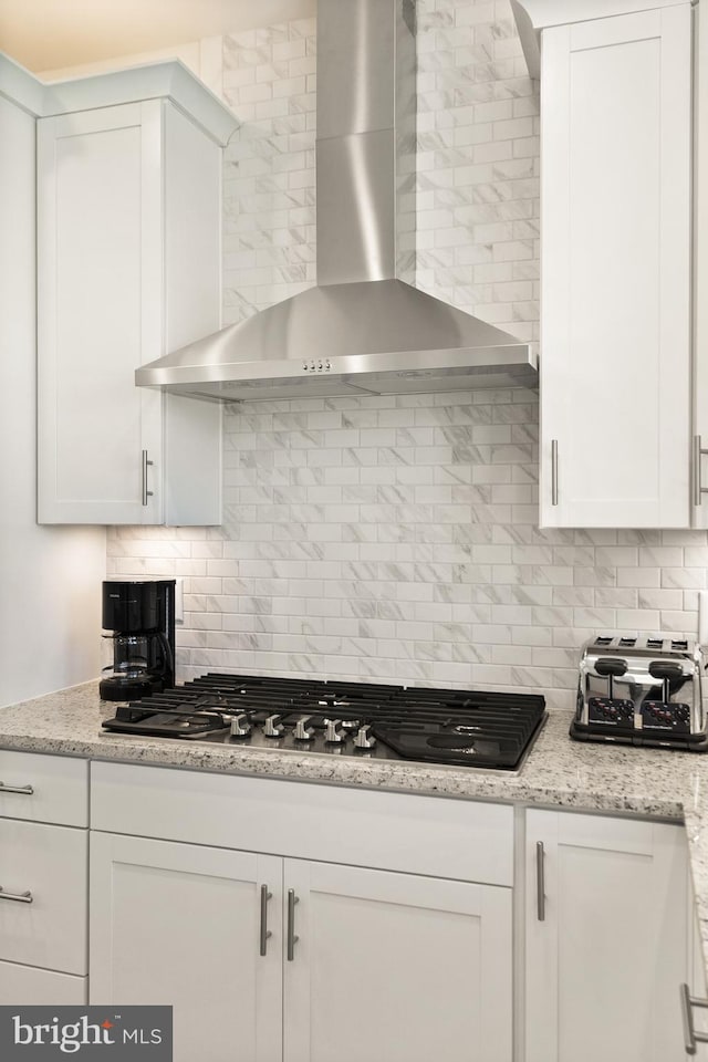 kitchen featuring stainless steel gas stovetop, tasteful backsplash, wall chimney exhaust hood, and white cabinetry
