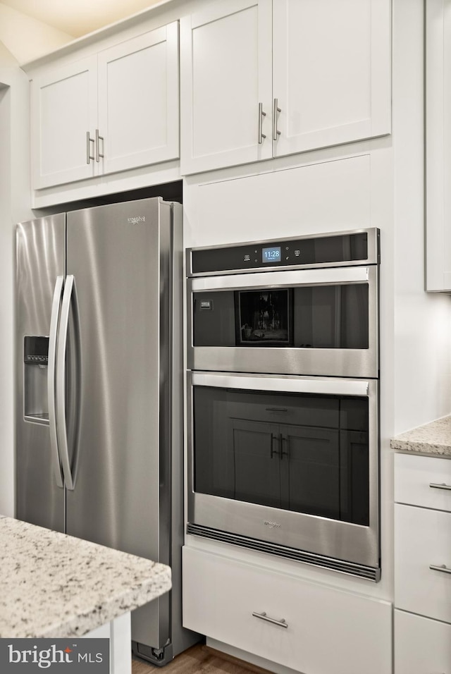 kitchen with white cabinets, appliances with stainless steel finishes, light stone counters, and wood finished floors