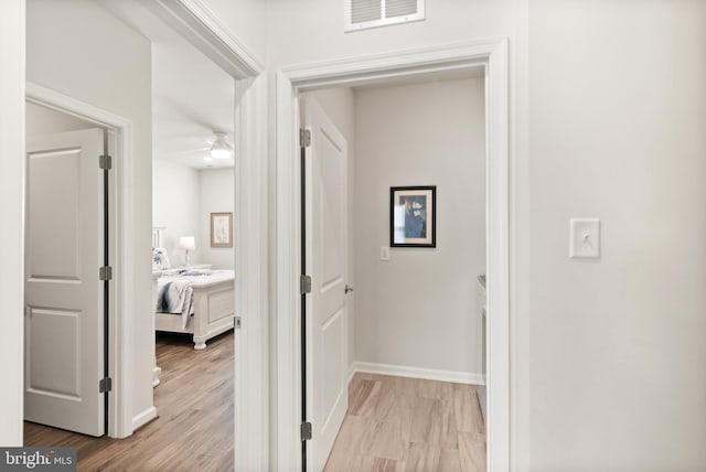 hallway featuring baseboards, light wood-type flooring, and visible vents