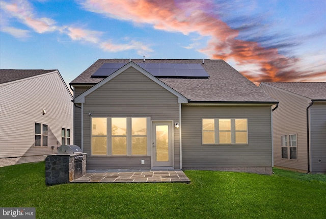 rear view of property featuring a yard, exterior kitchen, roof mounted solar panels, and roof with shingles