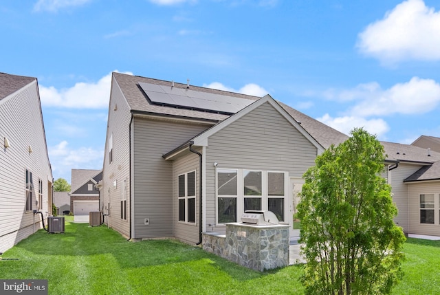 back of property featuring roof with shingles, an outdoor kitchen, roof mounted solar panels, central air condition unit, and a yard