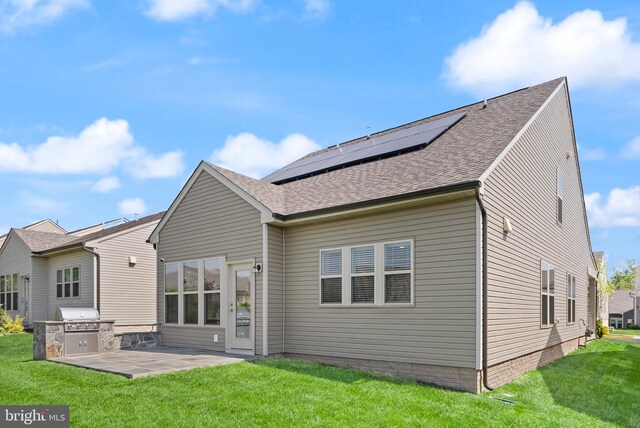 back of house with roof with shingles, an outdoor kitchen, roof mounted solar panels, a patio area, and a yard