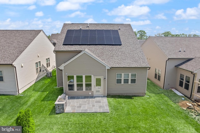 rear view of house featuring roof with shingles, a patio, a lawn, and roof mounted solar panels