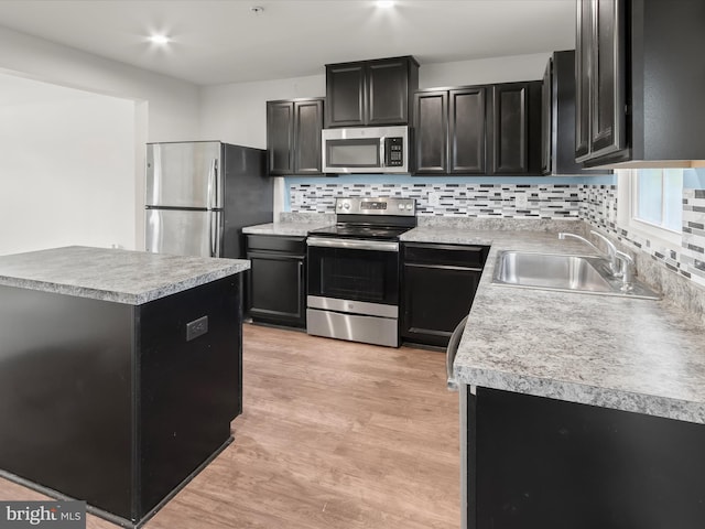 kitchen featuring backsplash, appliances with stainless steel finishes, a sink, light wood finished floors, and dark cabinetry