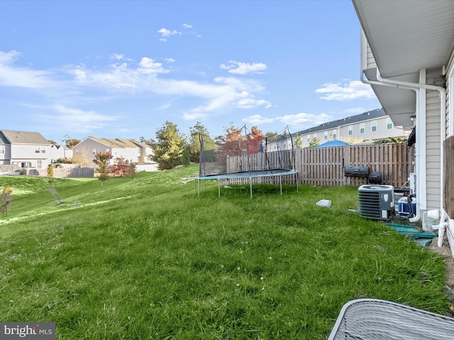 view of yard featuring central air condition unit, fence, a residential view, and a trampoline
