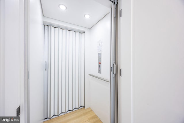 corridor with light wood-type flooring, recessed lighting, and elevator