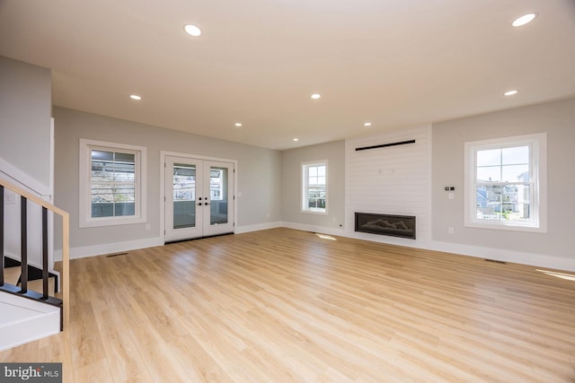 unfurnished living room featuring baseboards, light wood-style flooring, stairs, and a large fireplace