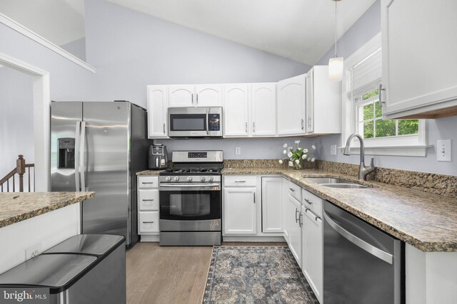 kitchen with white cabinets, a sink, light wood-style flooring, stainless steel appliances, and stone counters