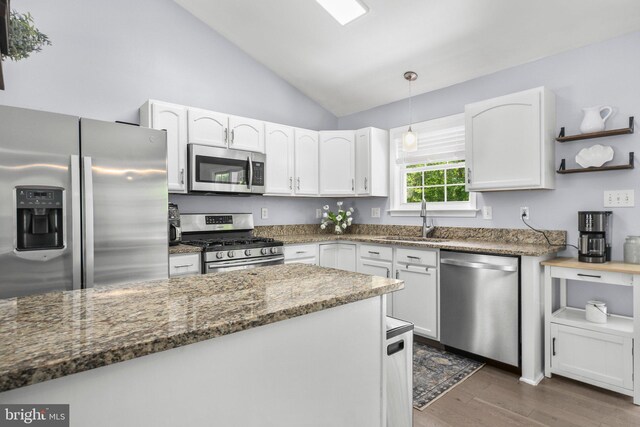 kitchen featuring lofted ceiling, white cabinetry, a sink, dark stone countertops, and appliances with stainless steel finishes