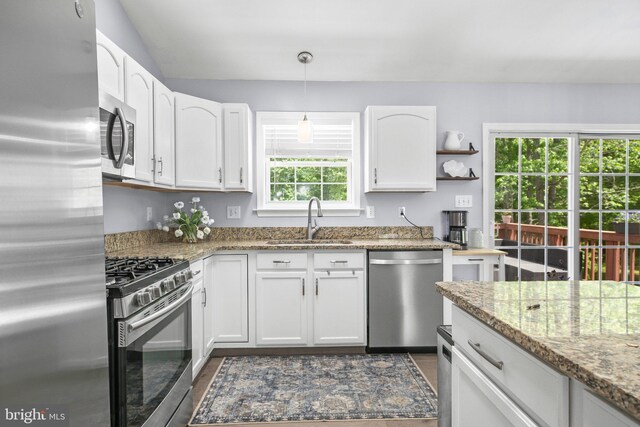 kitchen with white cabinets, stainless steel appliances, light stone counters, and a sink