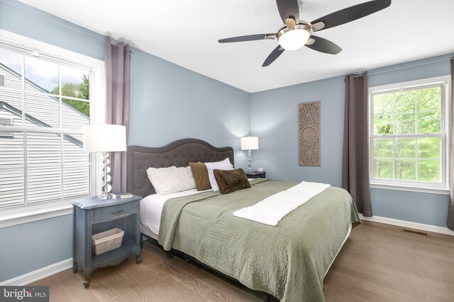 bedroom with a ceiling fan, baseboards, visible vents, and wood finished floors