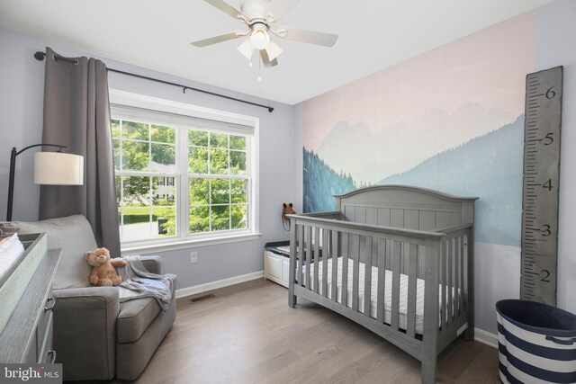 bedroom with visible vents, wood finished floors, baseboards, ceiling fan, and a nursery area
