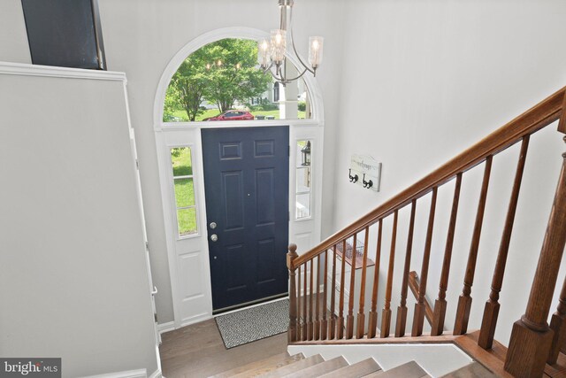 entryway with stairs, an inviting chandelier, a wealth of natural light, and wood finished floors