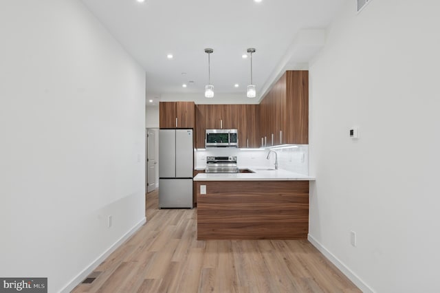 kitchen with backsplash, appliances with stainless steel finishes, light wood-type flooring, brown cabinets, and a peninsula