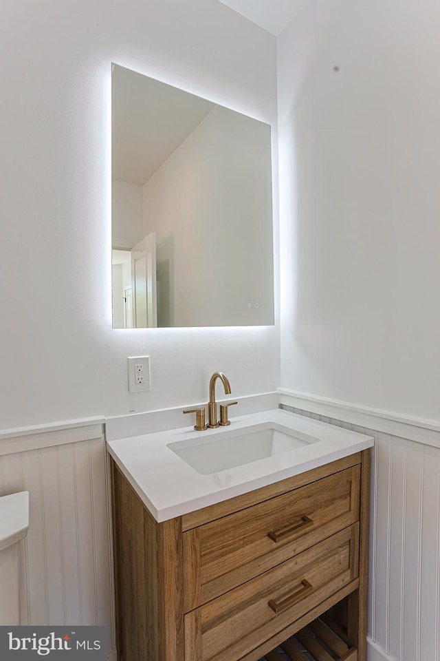 bathroom with vanity, wainscoting, a decorative wall, and toilet