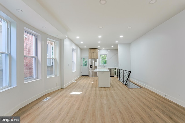 kitchen featuring visible vents, a kitchen island, baseboards, stainless steel refrigerator with ice dispenser, and light wood finished floors