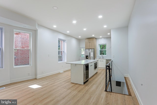 kitchen featuring stainless steel fridge, a center island, light wood-style flooring, and beverage cooler