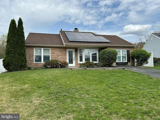 view of front of home with roof with shingles, a chimney, solar panels, and a front lawn