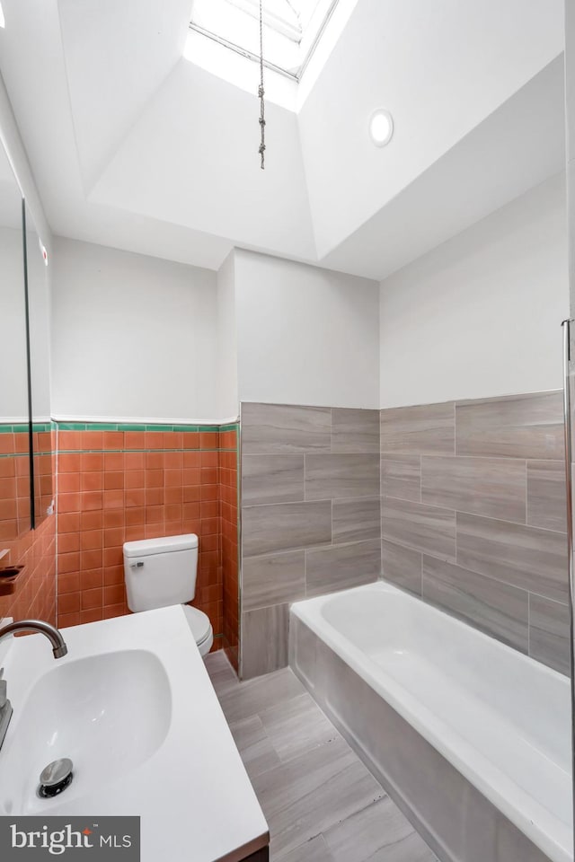 bathroom featuring a sink, toilet, a wainscoted wall, tile walls, and a tub to relax in