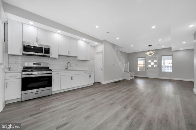 kitchen with a sink, stainless steel appliances, open floor plan, baseboards, and tasteful backsplash