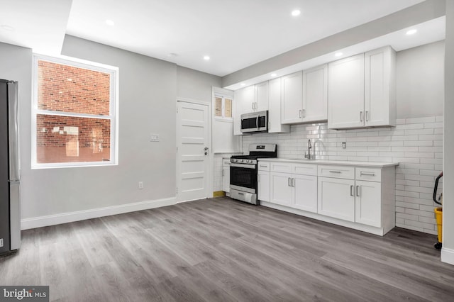 kitchen featuring decorative backsplash, wood finished floors, light countertops, a sink, and appliances with stainless steel finishes