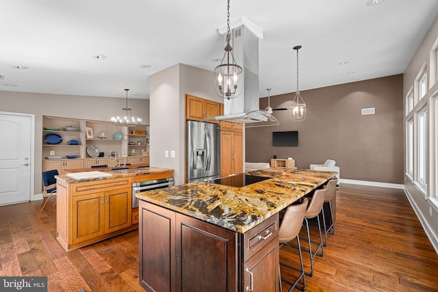 kitchen featuring a kitchen island, appliances with stainless steel finishes, dark wood finished floors, light stone counters, and an inviting chandelier