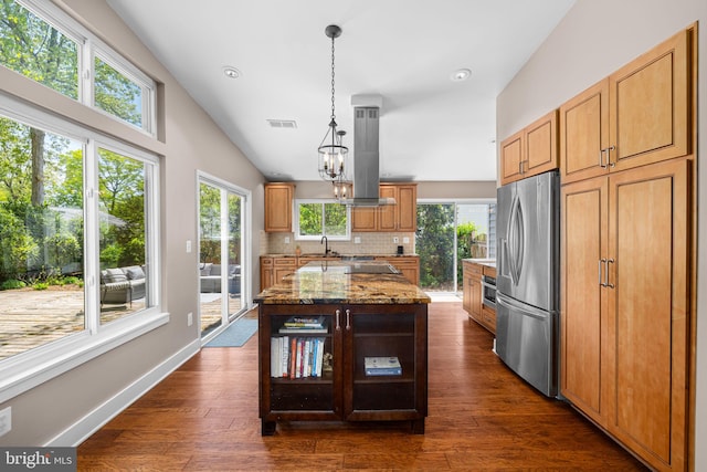 kitchen with island range hood, stainless steel fridge, light stone counters, a sink, and backsplash