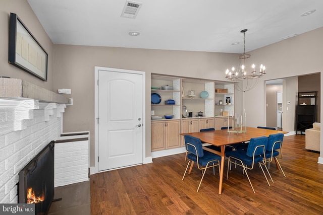 dining space with a chandelier, dark wood finished floors, visible vents, and a fireplace