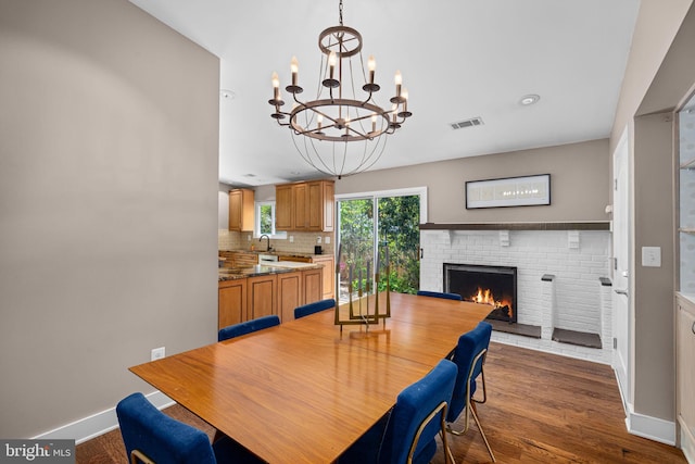 dining space featuring a notable chandelier, a fireplace, baseboards, dark wood-type flooring, and visible vents