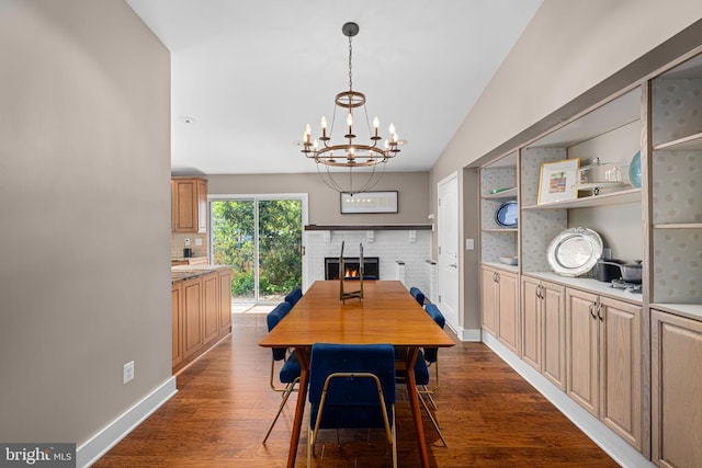 dining area featuring an inviting chandelier, a brick fireplace, lofted ceiling, baseboards, and dark wood finished floors