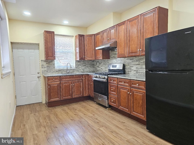 kitchen with a sink, light wood finished floors, stainless steel gas stove, freestanding refrigerator, and under cabinet range hood
