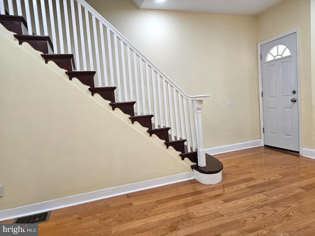 foyer entrance with stairway, baseboards, wood finished floors, and visible vents