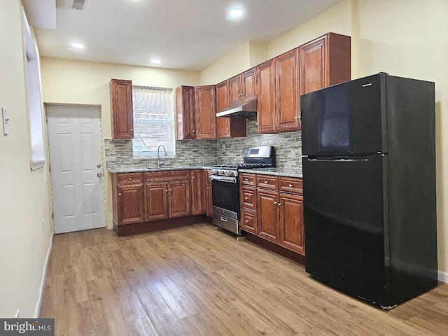 kitchen featuring a sink, light wood-style floors, stainless steel gas stove, freestanding refrigerator, and under cabinet range hood