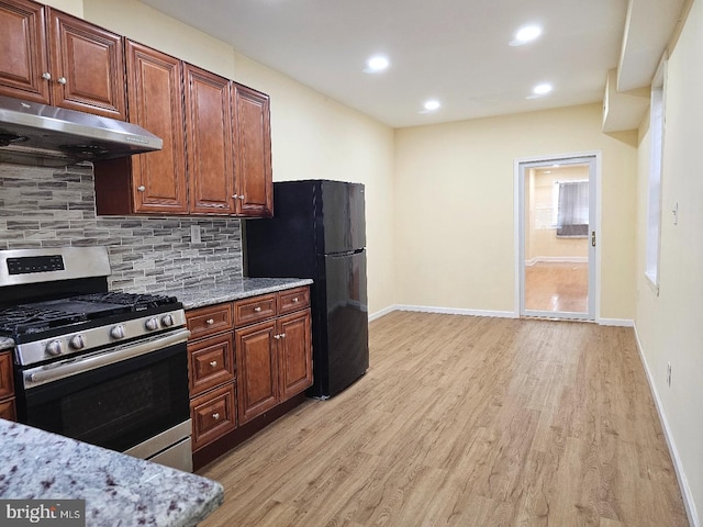 kitchen with freestanding refrigerator, decorative backsplash, stainless steel gas stove, light wood-style floors, and under cabinet range hood