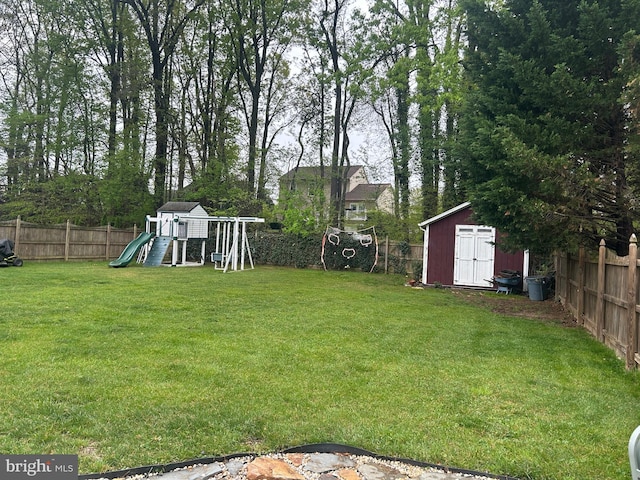view of yard with a storage unit, a fenced backyard, a playground, and an outdoor structure