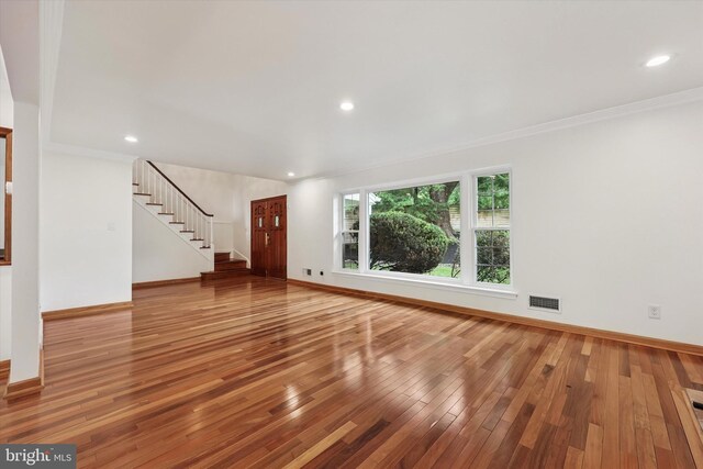 unfurnished living room featuring hardwood / wood-style flooring, stairway, baseboards, crown molding, and recessed lighting