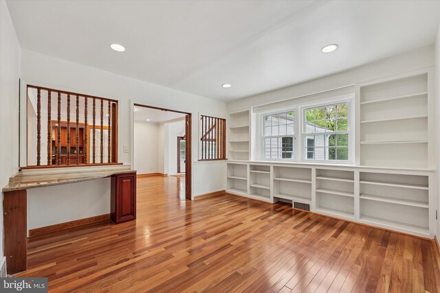unfurnished room with wood finished floors, built in shelves, recessed lighting, and baseboards