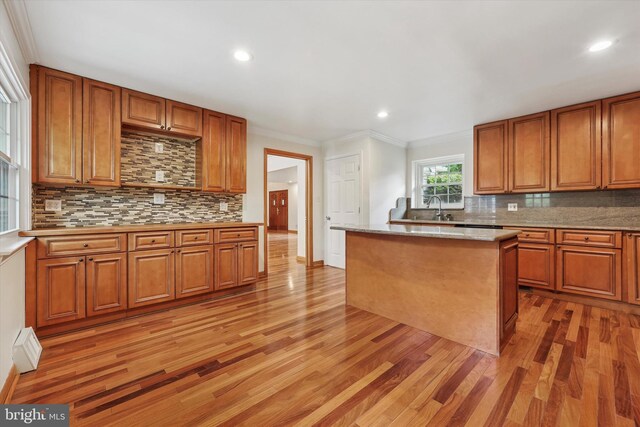kitchen featuring light wood-style floors, decorative backsplash, brown cabinets, recessed lighting, and crown molding