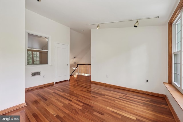 empty room with wood finished floors, rail lighting, and baseboards