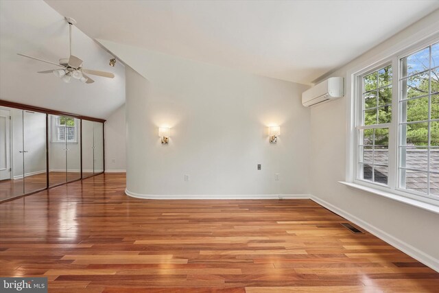spare room with an AC wall unit, a ceiling fan, lofted ceiling, baseboards, and light wood-type flooring