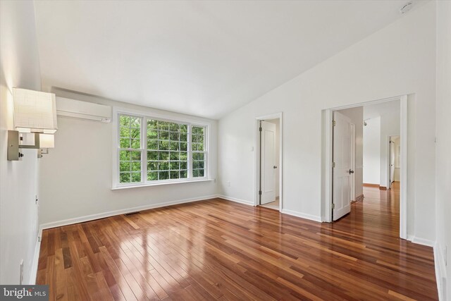 empty room with an AC wall unit, lofted ceiling, hardwood / wood-style flooring, baseboards, and a smoke detector