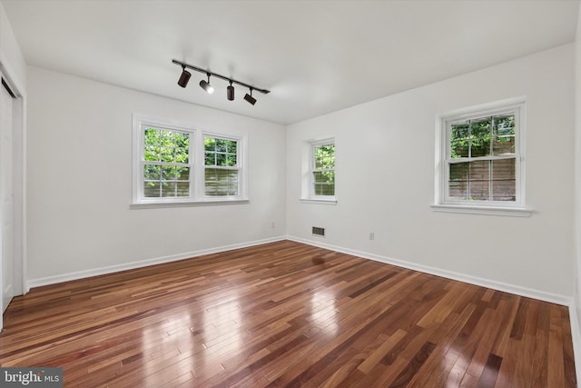 empty room featuring track lighting, wood-type flooring, and baseboards