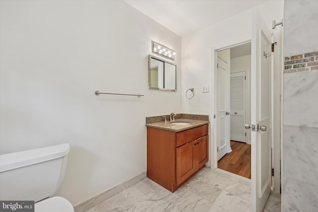 bathroom with baseboards, marble look tile flooring, vanity, and toilet