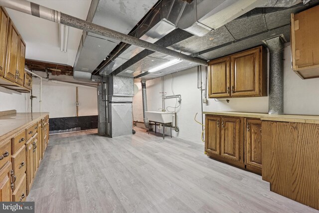 unfinished basement with light wood-style floors, a sink, and heating unit