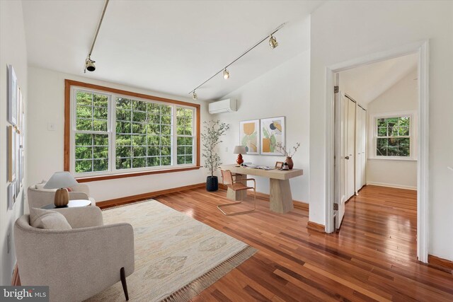 living area featuring rail lighting, a wall mounted AC, wood finished floors, baseboards, and lofted ceiling